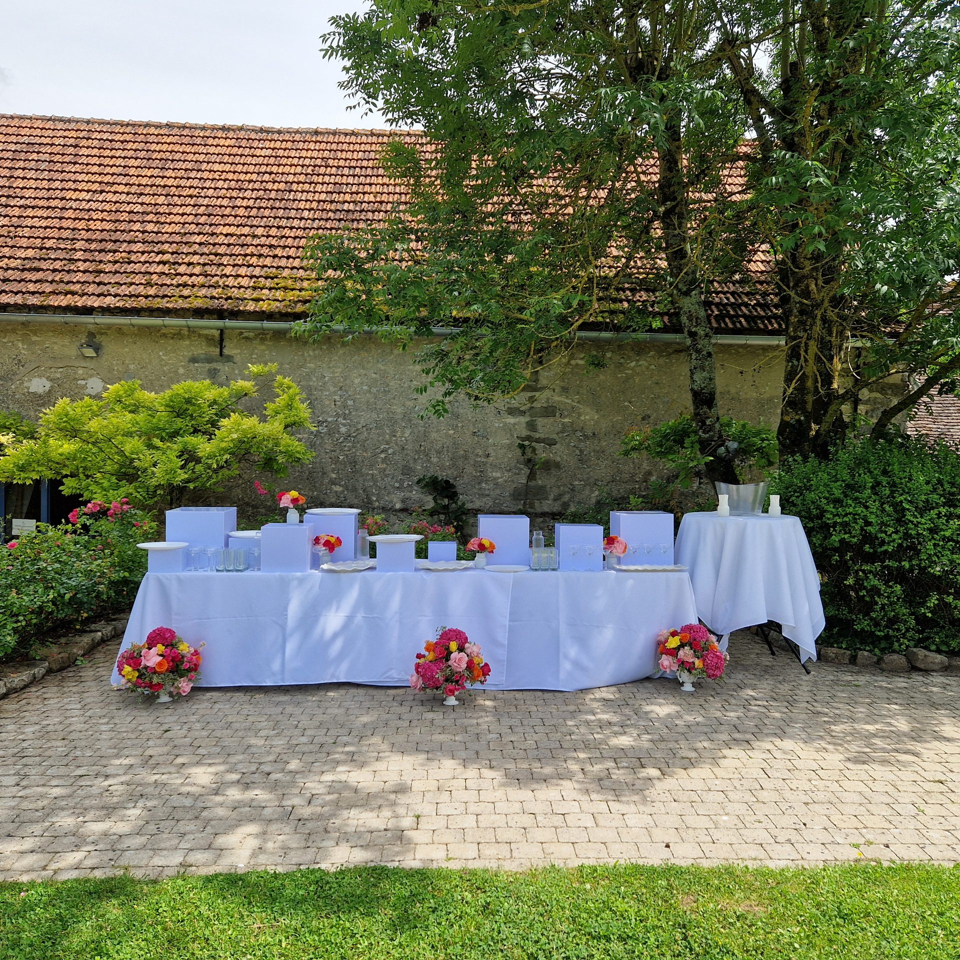 Table d'accueil fleurie dans la cour, devant les bâtiments en pierre