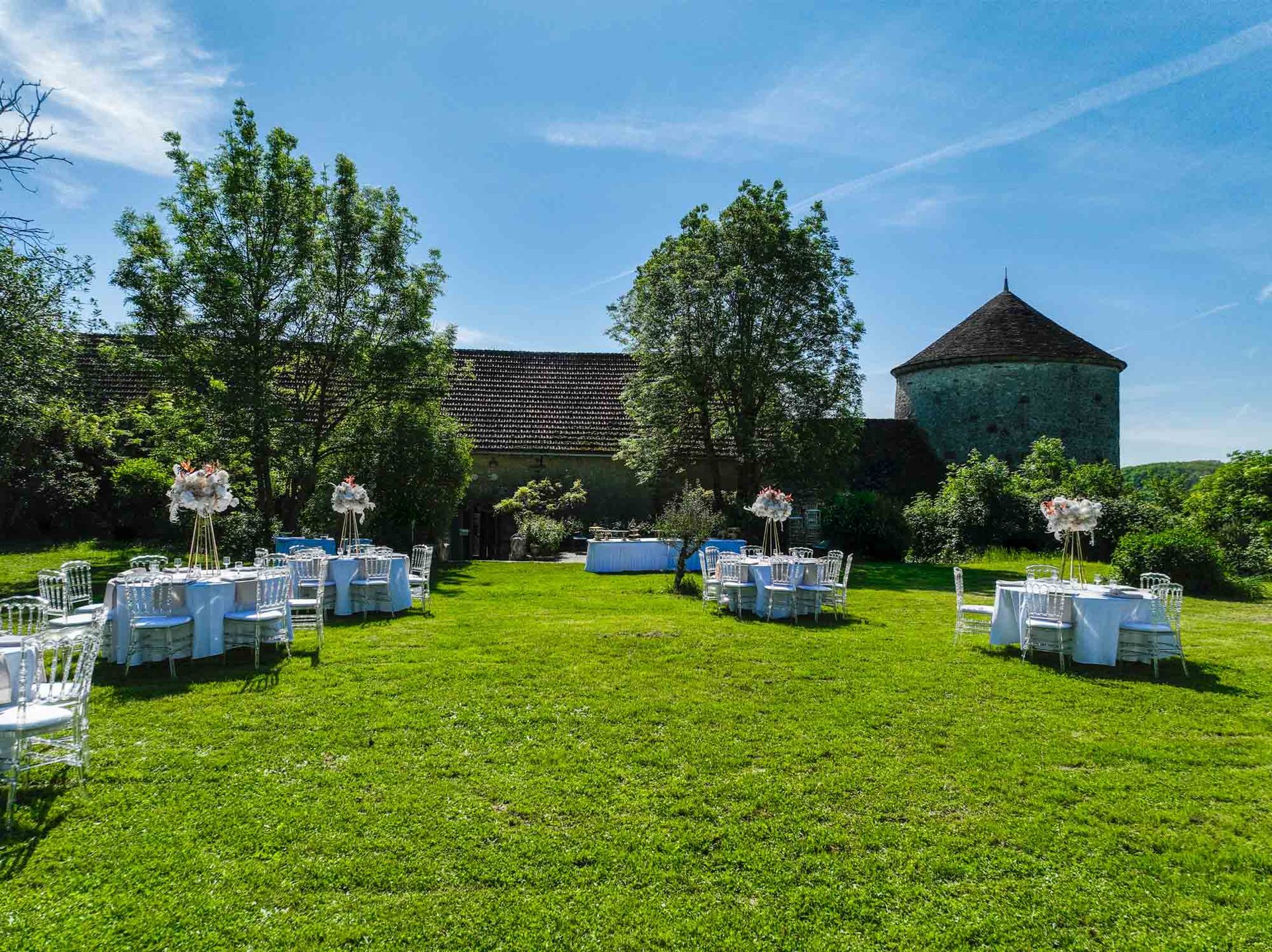 Réception en extérieur devant la grange et le pigeonnier — tables et compositions florales